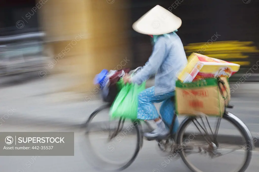 Female vendor on a bicycle in a street, Hoi An, Vietnam