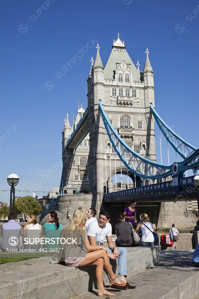 Tourists sitting near a bridge, Tower Bridge, Thames River, London, England