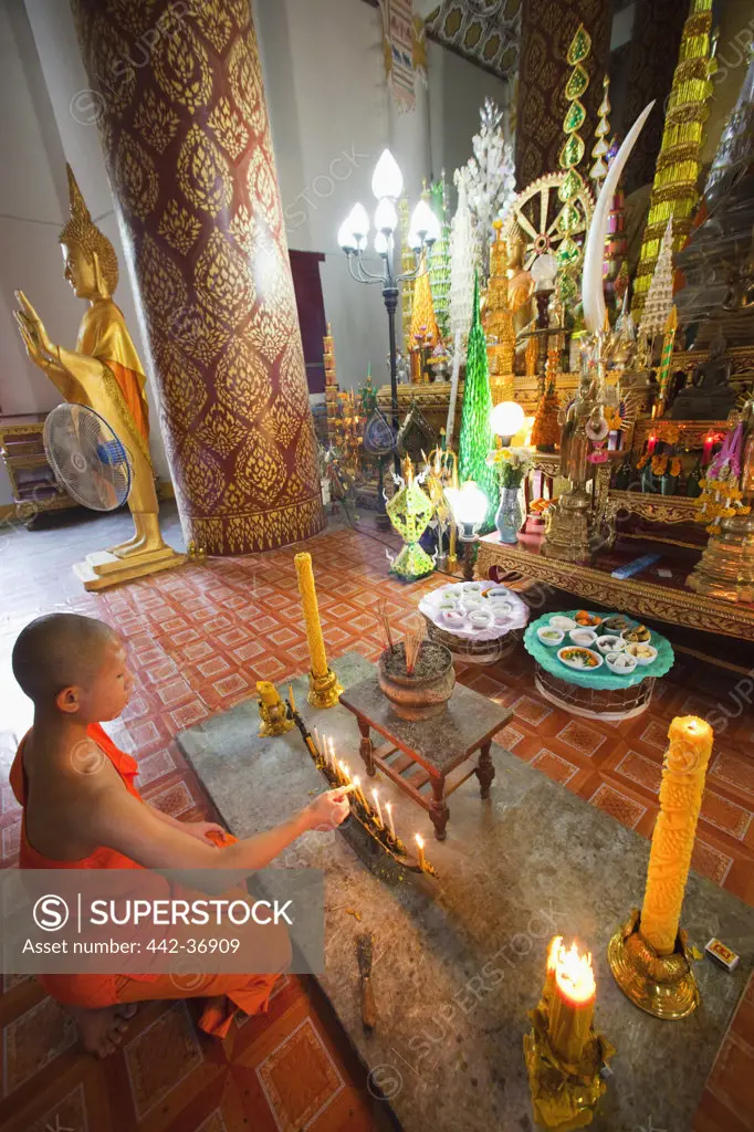 Monk lighting votive candles in the main prayer hall, Wat Inpeng, Vientiane, Laos
