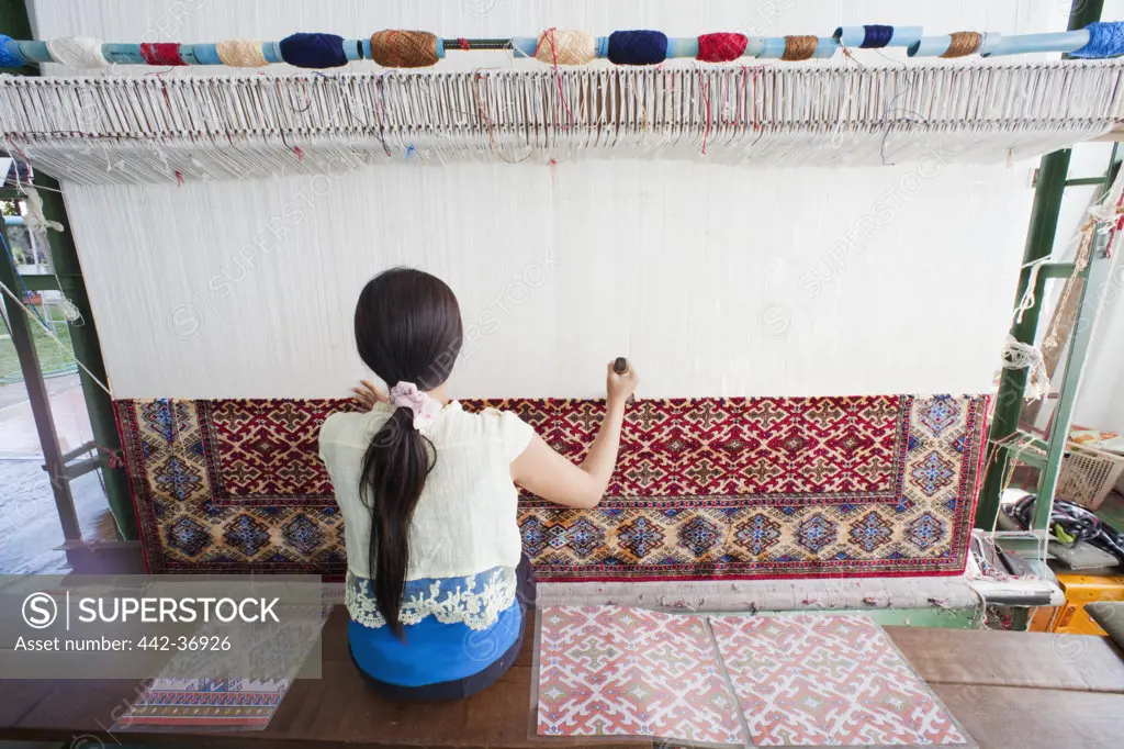 Woman weaving carpet in a loom, Thailand