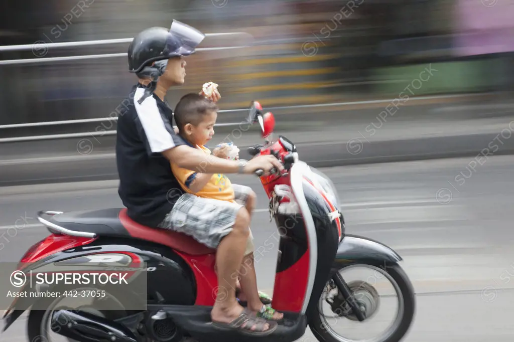 Man riding motor cycle with his son on street, Bangkok, Thailand