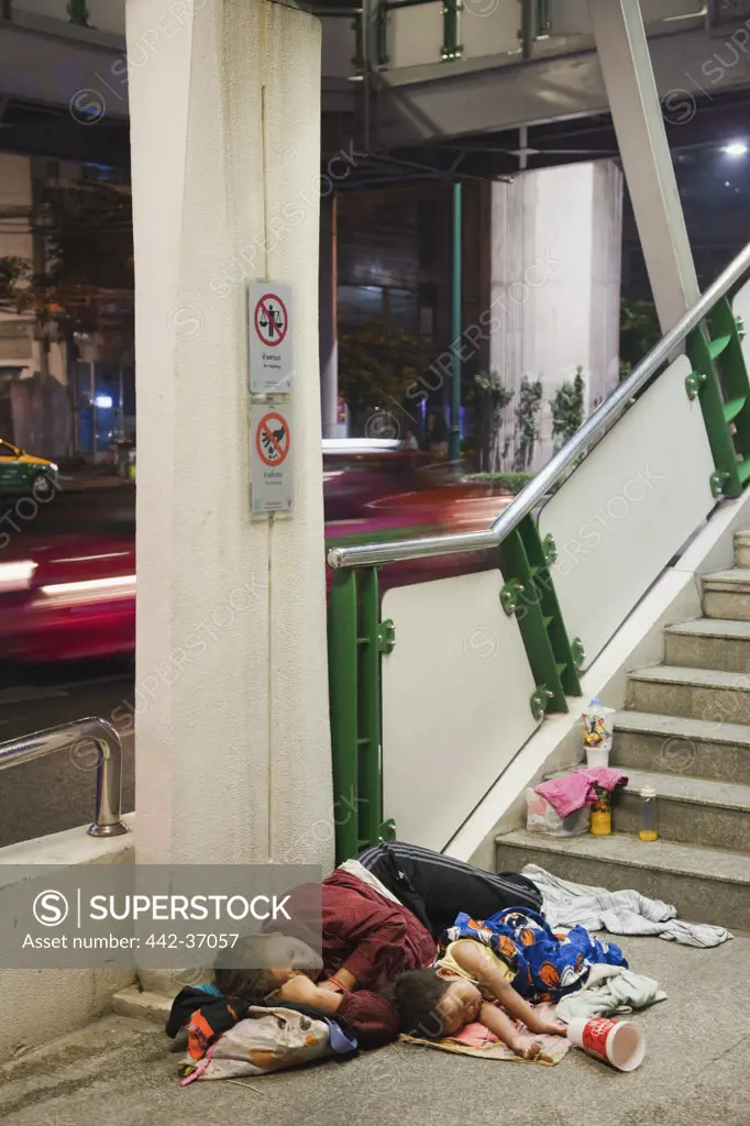 Homeless woman sleeping with daughter near the steps of a footbridge, Bangkok, Thailand
