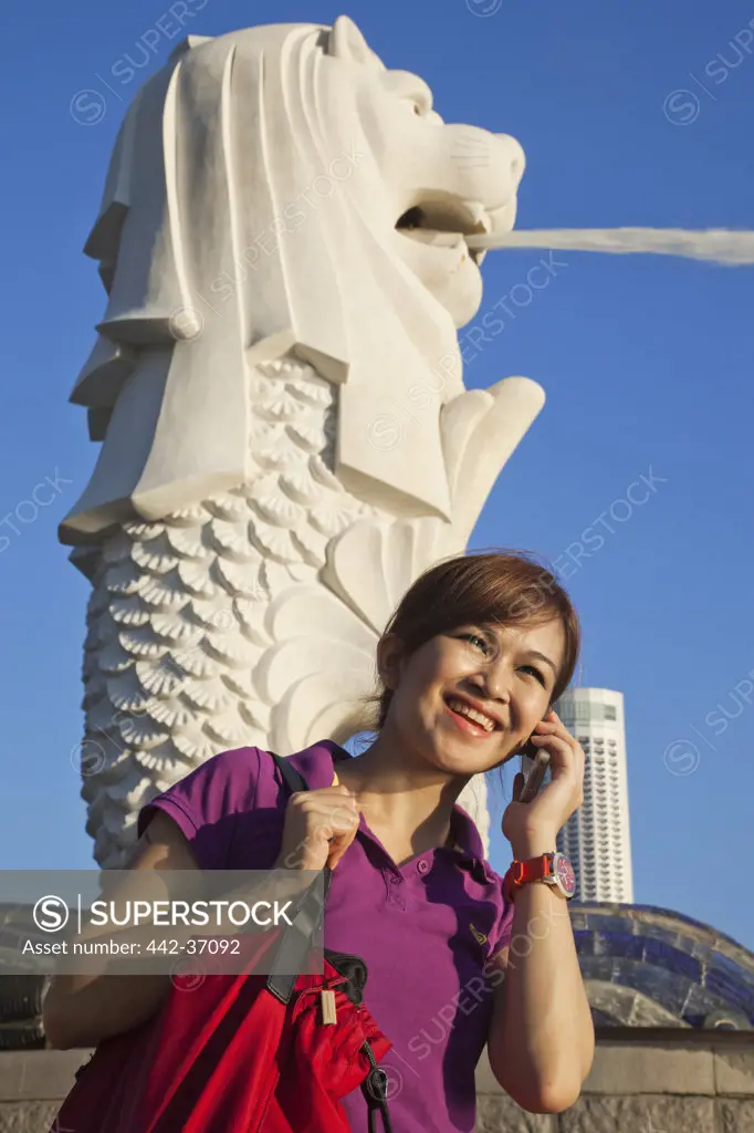 Woman talking on a mobile phone in front of the Merlion Statue, Singapore City, Singapore