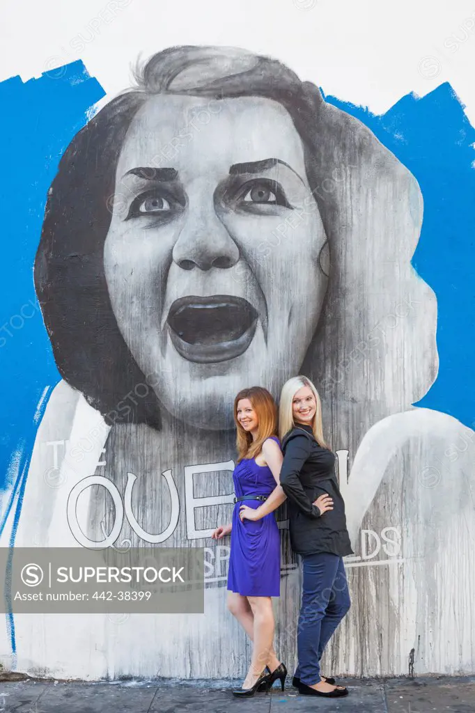 Two women posing in front of a graffiti, Shoreditch, London, England