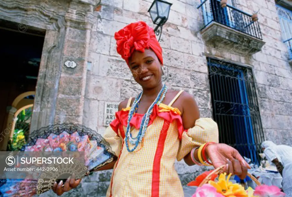 Young woman in a traditional dress holding a fan and a basket of flowers, Havana, Cuba