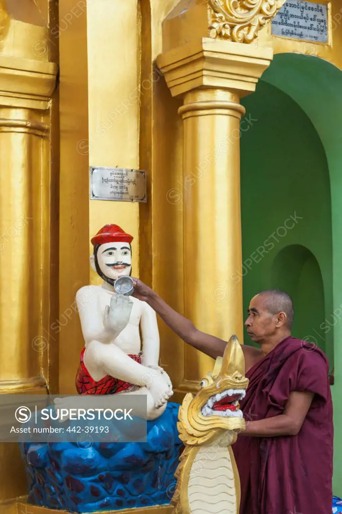 Monk pouring holy water on statue, Shwedagon Pagoda, Yangon, Myanmar