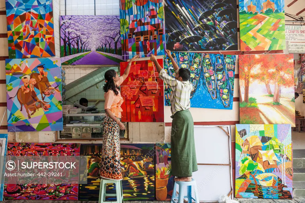 Man and woman hanging paintings in a shop, Bogyoke Market, Yangon, Myanmar