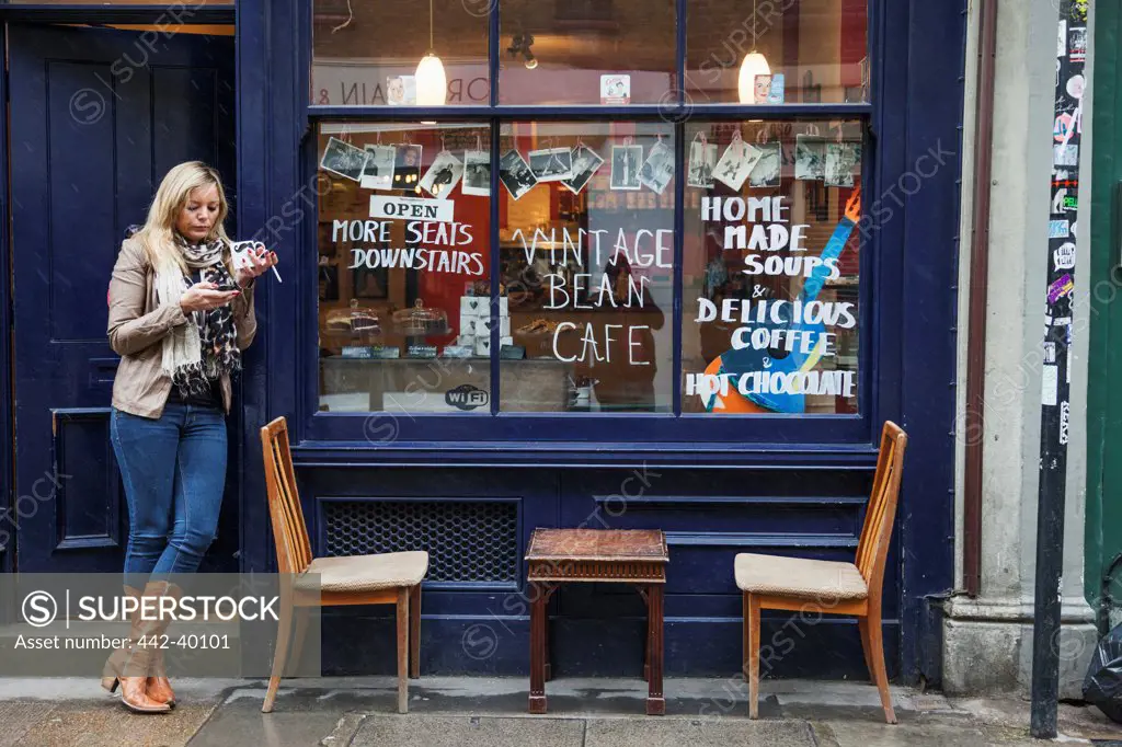 UK, England, London, Shoreditch, Brick Lane, Woman smoking outside coffee shop