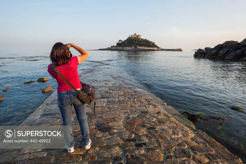 Woman taking picture of a castle on the island from the jetty, St. Michael's Mount, Marazion, Cornwall, England