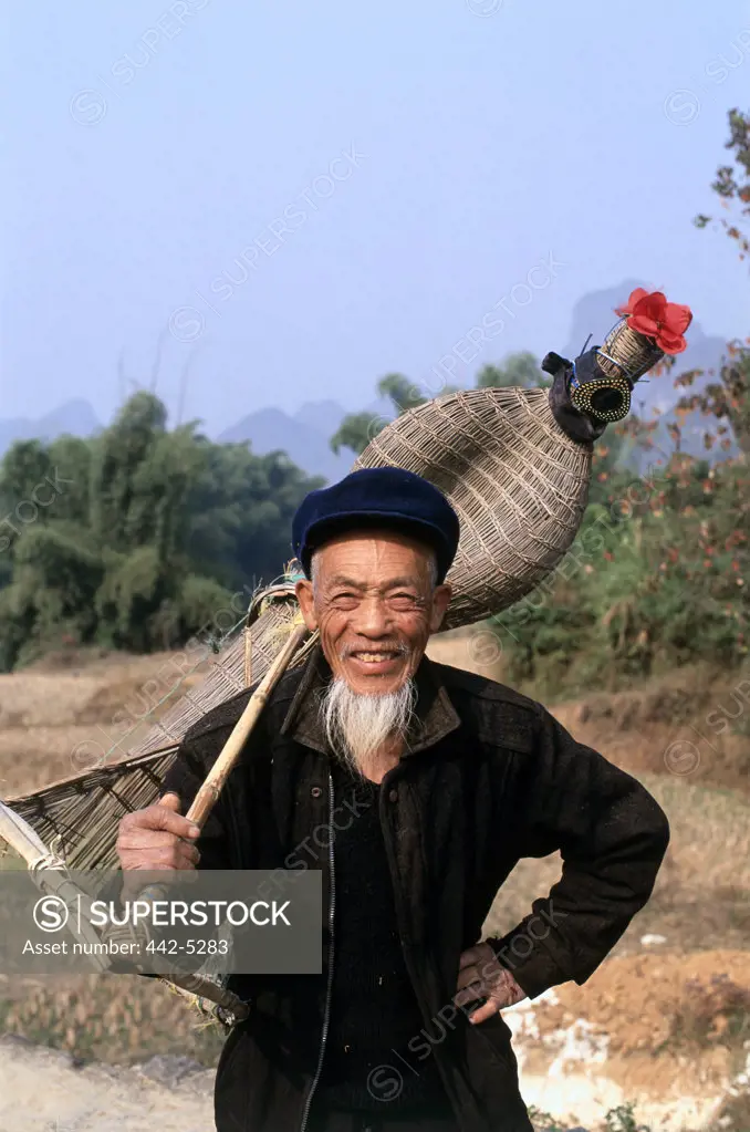 Portrait of a mature man holding fishing equipment, Yangshou, China