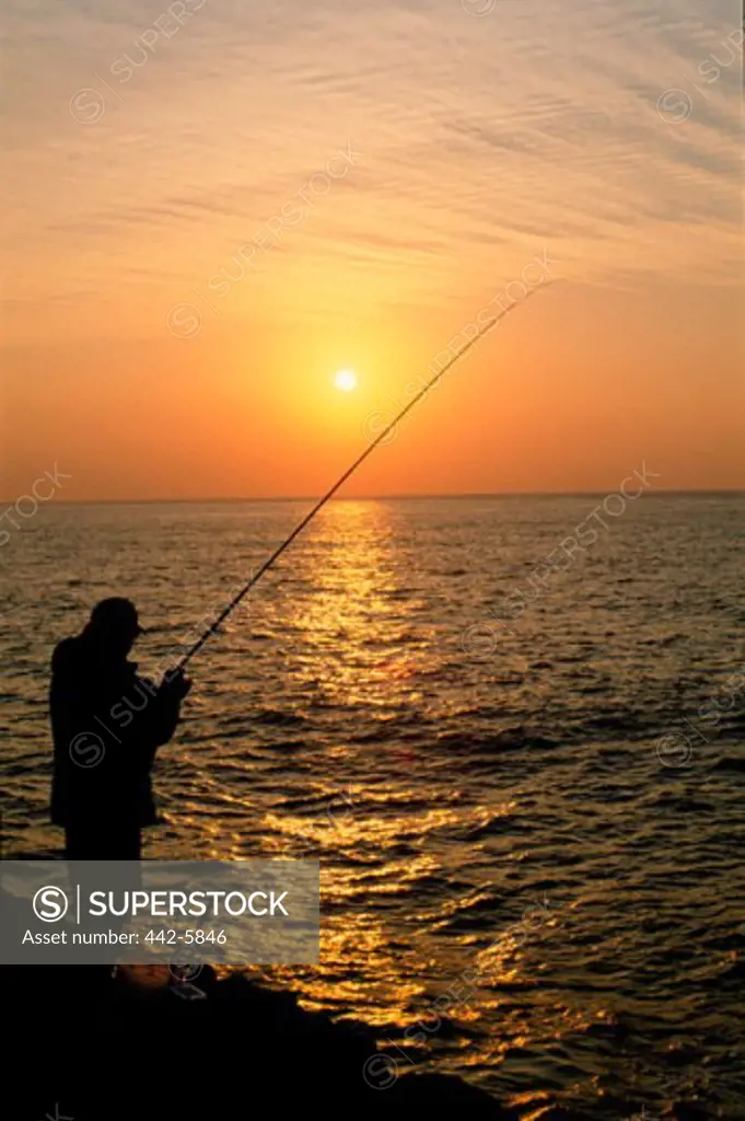 Silhouette of a fisherman fishing at sunset