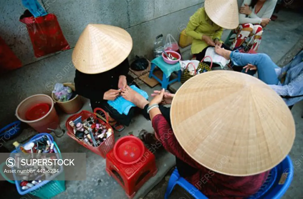 High angle view of two women wearing traditional conical hats getting pedicures, Can Tho, Vietnam