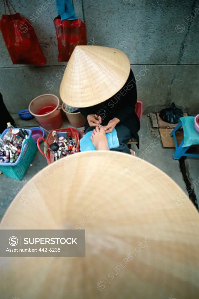 High angle view of a woman wearing a traditional conical hat getting a pedicure, Can Tho, Vietnam