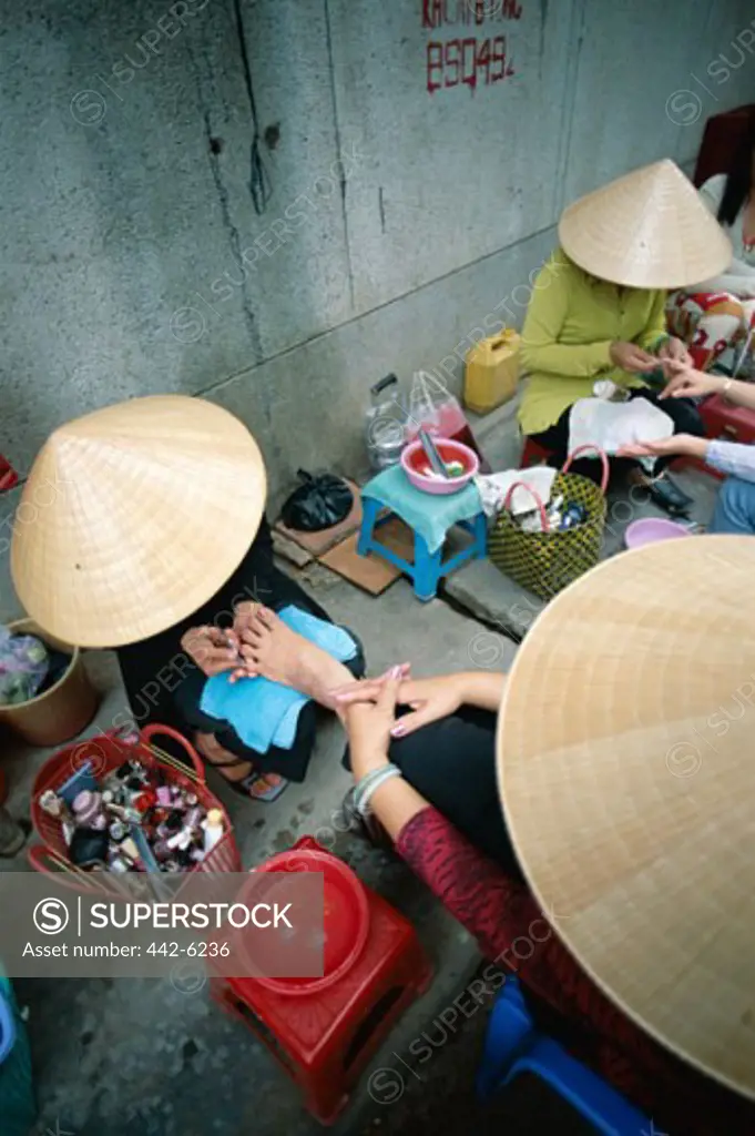 High angle view of two women wearing traditional conical hats getting a manicure and a pedicure, Can Tho, Vietnam