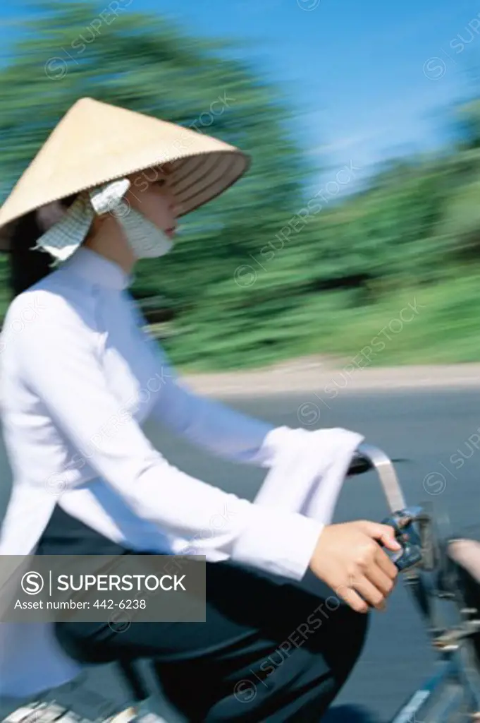 Side profile of a teenage girl wearing a traditional conical hat cycling, Vietnam