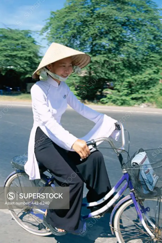 Side profile of a teenage girl wearing a traditional conical hat cycling, Vietnam