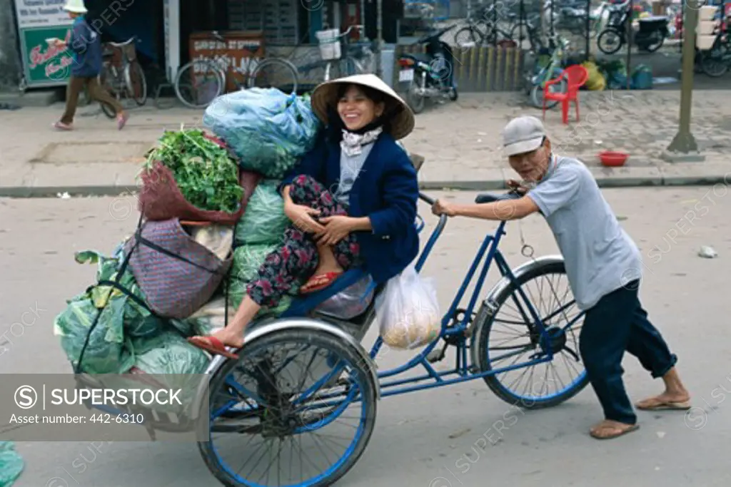 Mid adult woman sitting in a rickshaw with market produce in a street market, Hue, Vietnam