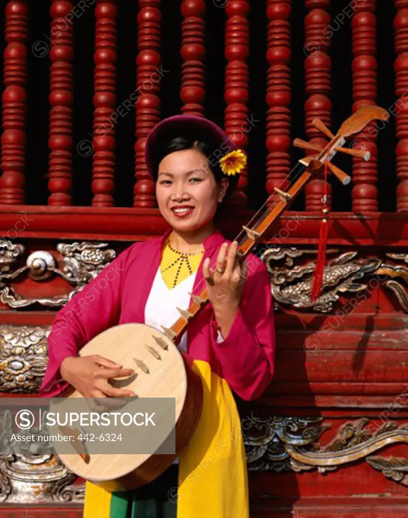 Portrait of a young woman dressed in a traditional costume playing a musical instrument, Temple of Literature, Hanoi, Vietnam