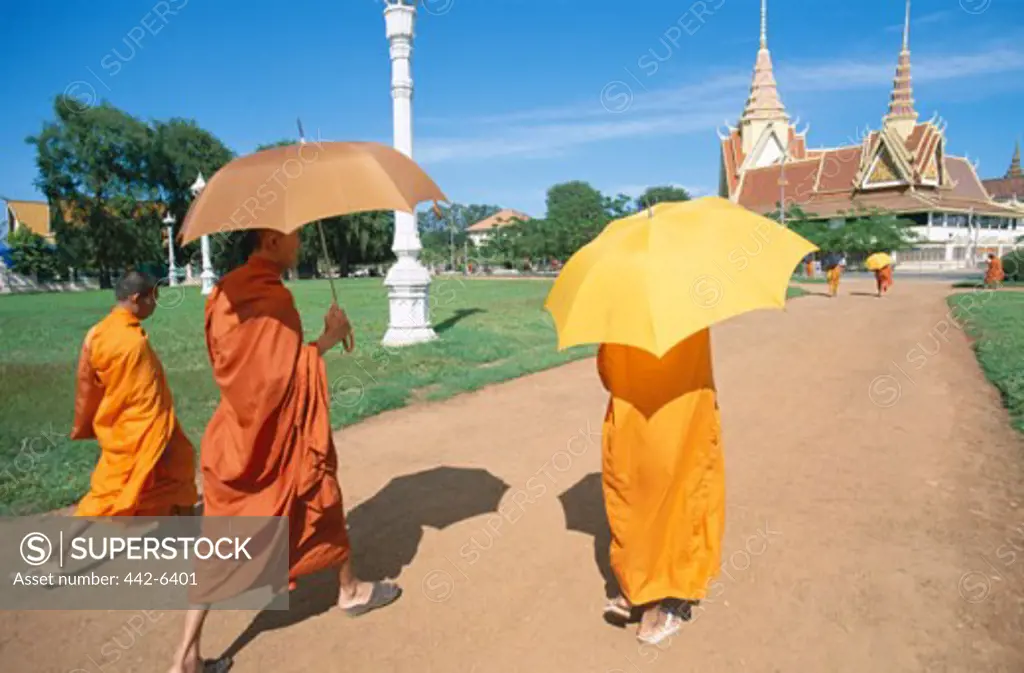 Rear view of three monks walking with umbrellas, Phnom Penh, Cambodia