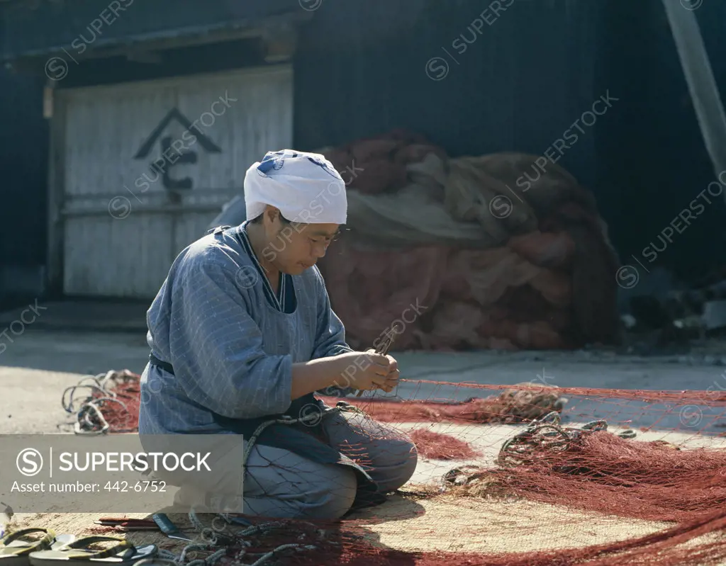 Mid adult woman repairing a fishing net, Honshu, Japan