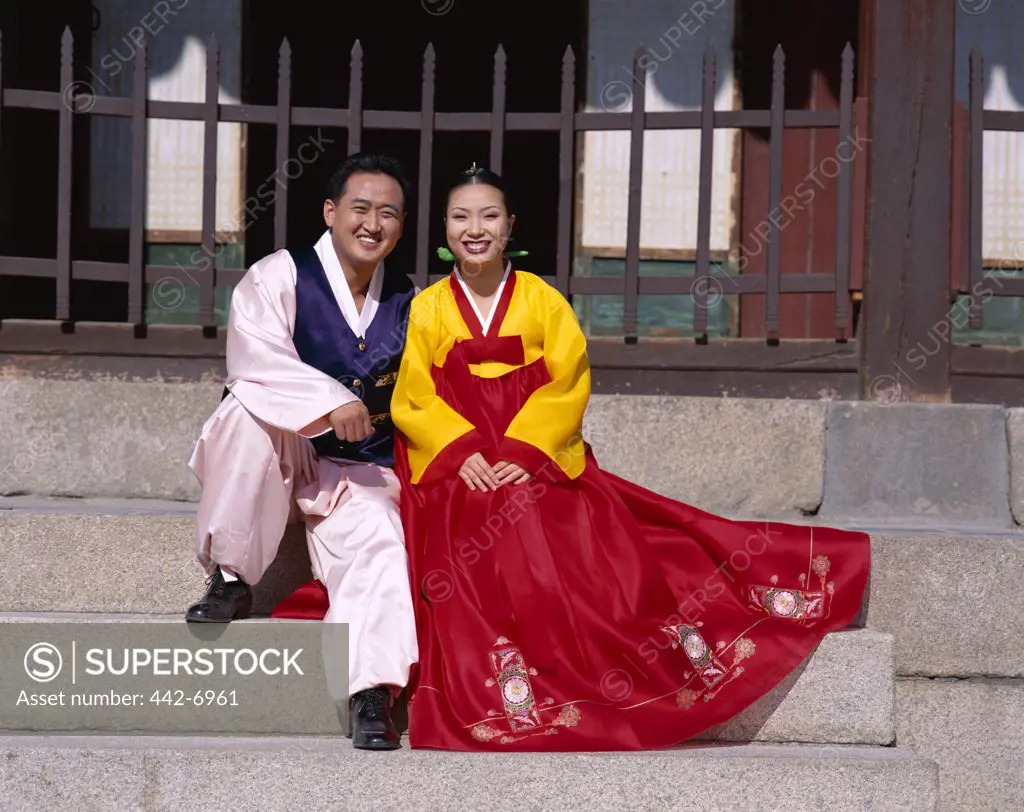 Portrait of a newlywed couple dressed in traditional wedding costumes sitting on steps, Kyongbokkung Palace, Seoul, South Korea