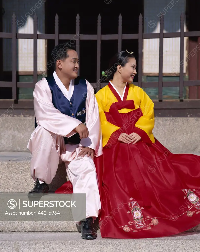 Newlywed couple dressed in traditional wedding costumes sitting on steps, Kyongbokkung Palace, Seoul, South Korea