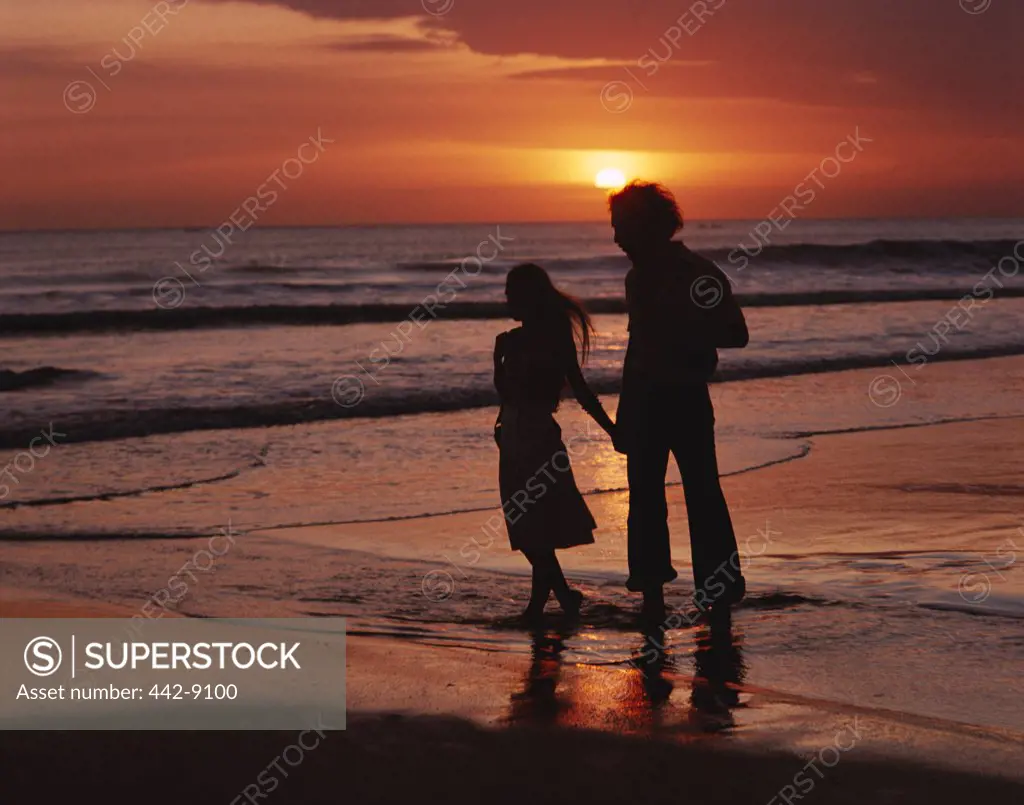 Silhouette of a young couple walking on the beach during sunset, Bali, Indonesia
