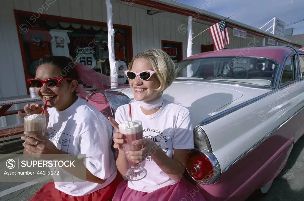Two teenage girls leaning against a car with ice cream floats, Twisters Soda Fountain, Route 66, Williams, Arizona, USA