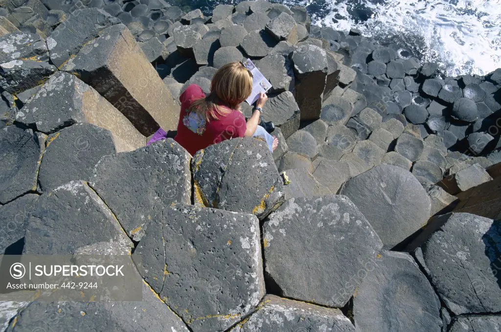 High angle view of a woman sitting on rocks, Giants Causeway, County Antrim, Northern Ireland