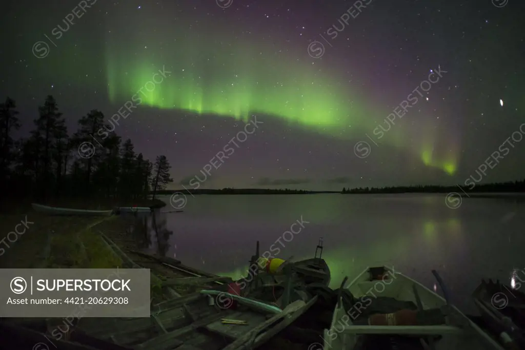 Aurora Borealis and stars over lake with beached canoes at night, Muonio, Lapland, Finland, September 