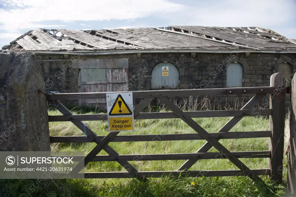 ''Danger, Keep out'' sign on gate and derelict farm building, Lancashire, England, April 
