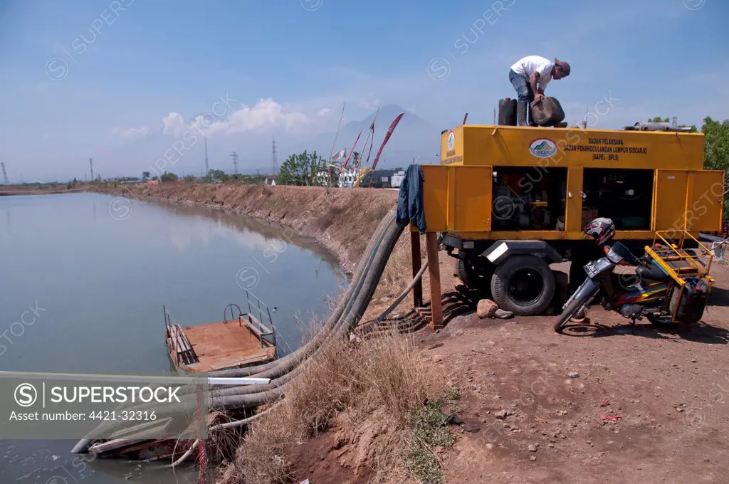 Worker on levee using water pump to drain mud lake of mud volcano, environmental disaster which developed after drilling incident, Porong Sidoarjo, near Surabaya, East Java, Indonesia