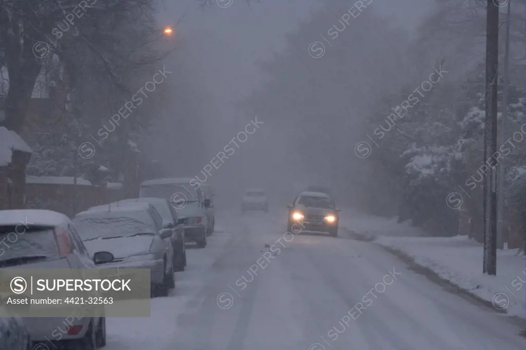 Cars driving in heavy snowfall, with headlights and street lamps on, along snow covered road, Ipswich, Suffolk, England, january 2010