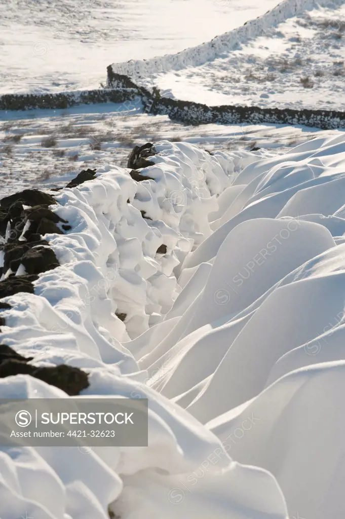 Snow patterns, formed by wind blown snow beside drystone wall, Peak District, Derbyshire, England, winter