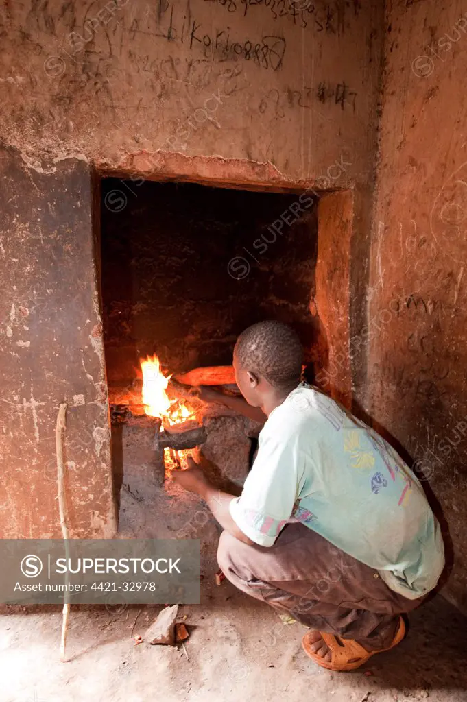Boy lighting kitchen stove in hut, Rwanda