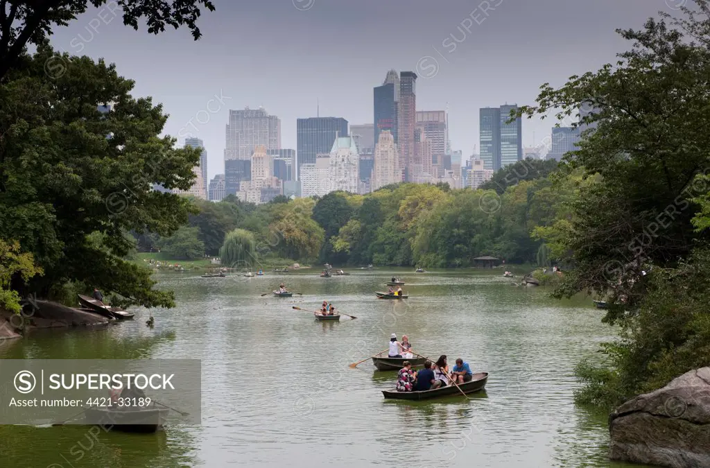 Tourists in rowing boats on boating lake in city parkland, with skyline of skyscrapers in background, Central Park, Manhattan Island, New York City, New York State, U.S.A., september
