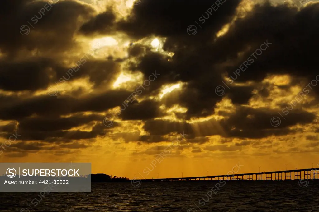 View of sunbeams over coast at sunset, with bridge to South Padre Island, Port Isabel, Texas, U.S.A., april