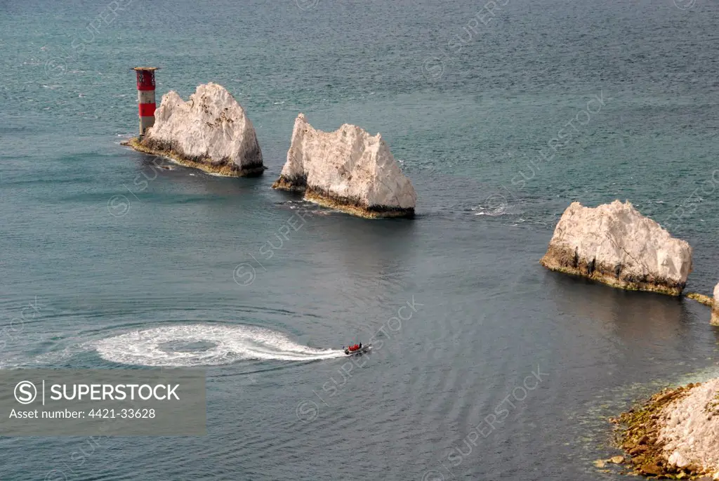 Row of chalk sea stacks and lighthouse, with speedboat taking sightseers on trip, The Needles, Isle of Wight, England