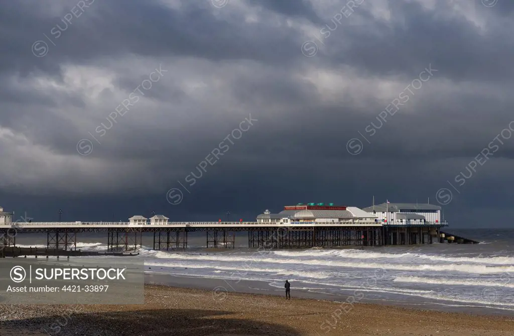 View of beach and pier of seaside town, with stormclouds overhead, Cromer Pier, Cromer, Norfolk, England, november