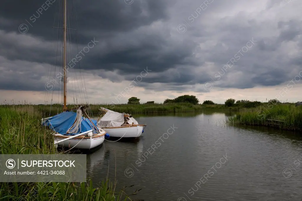 Boats moored under stormclouds, River Thurne, The Broads N.P., Norfolk, England, may