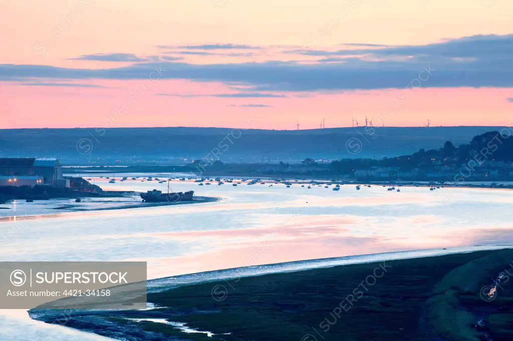 View of river estuary with shipyard, village and distant windfarm on banks at sunrise, Fullabrook Windfarm, Instow Village, Appledore Shipyard, River Torridge, North Devon, England, june