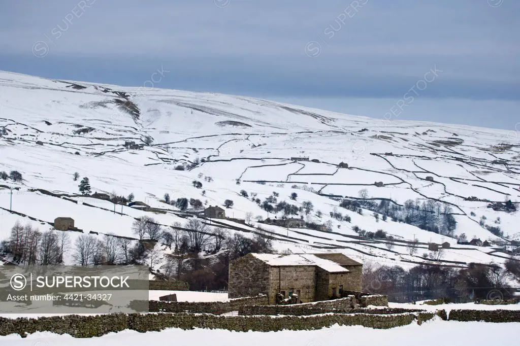 View of snow covered upland farmland with stone barns and drystone walls, Swaledale, Yorkshire Dales N.P., North Yorkshire, England, february