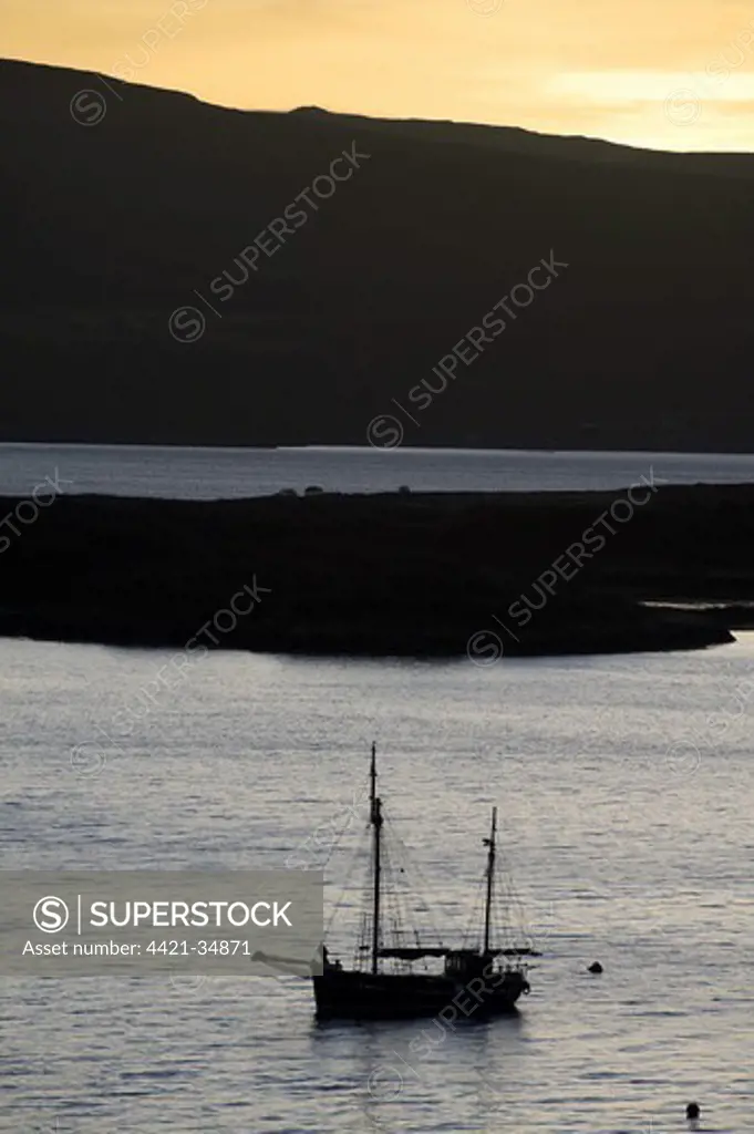 Boat silhouetted in bay at sunrise, Tobermory Bay, Isle of Mull, Inner Hebrides, Scotland