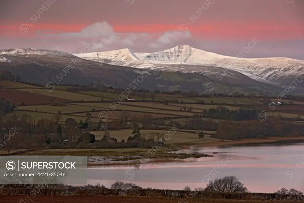 View of lake, farmland and snow covered hills at dawn, Llangorse Lake, Brecon Beacons N.P., Powys, Wales, january
