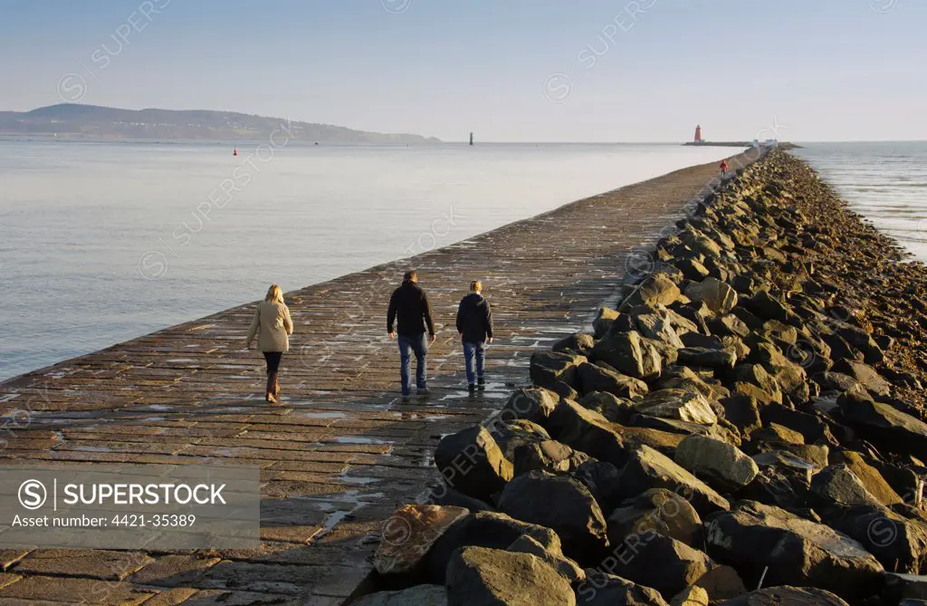 People walking on sea wall protecting harbour entrance, sea wall preventing sand encroachment from South Bull sandbank at Sandymount, Great South Wall, Dublin Port, Dublin Bay, Ireland, november