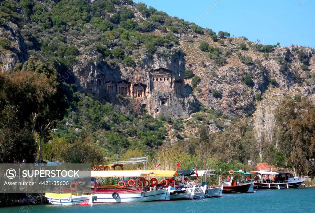 View of tourist boats on river and Lycian rock tombs (circa 400 BC) carved in cliff, Dalyan River, Mugla Province, Turkey, april