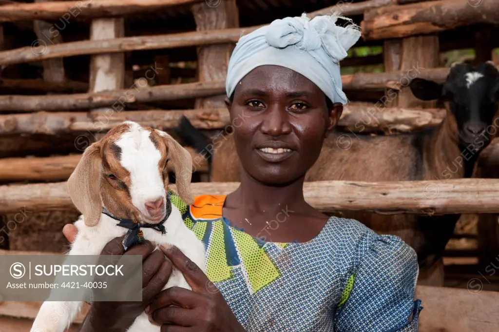 Goat farming, woman holding young Boer goat beside shed, Rwanda
