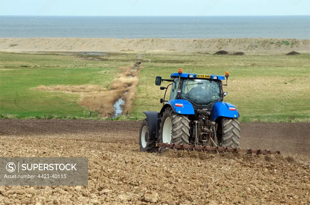 Tractor tilling soil in coastal arable farmland, with grazing marsh and sea in background, Salthouse, Norfolk, England, april