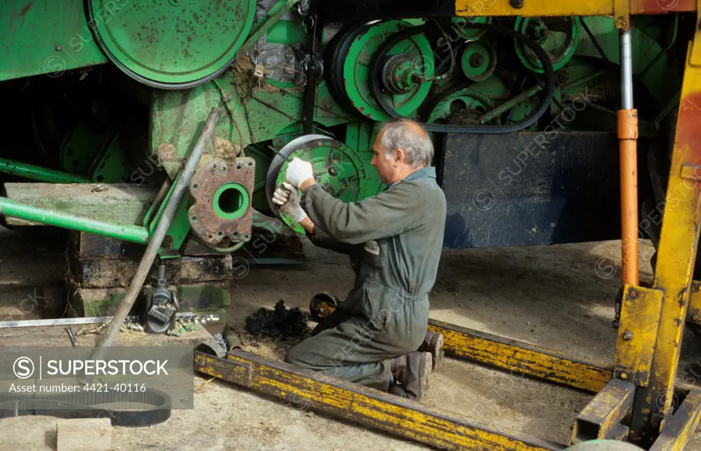 Farmer repairing combine harvester clutch at harvest time, West Sussex, England, august