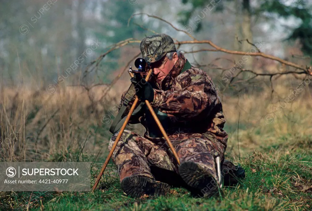 Hunting, deer stalker sitting on low seat and using tripod to support rifle, England